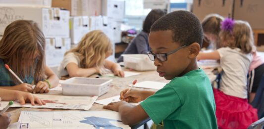 채플힐-캐보로 학군 예산 부족으로 5개 학교 폐교 검토 boy in green sweater writing on white paper