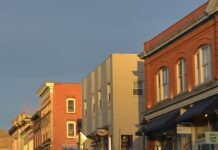 그린스보로, 상업용 건물 관리 강화… 한인 자영업자가 알아야 할 새 규정 Street with parked cars and brick buildings at sunset.