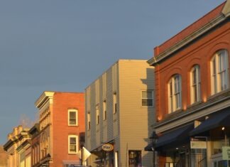 그린스보로, 상업용 건물 관리 강화… 한인 자영업자가 알아야 할 새 규정 Street with parked cars and brick buildings at sunset.